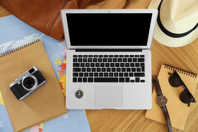 Flat lay composition with laptop and different items on wooden table. Trip planning