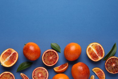Photo of Many ripe sicilian oranges and leaves on blue background, flat lay. Space for text