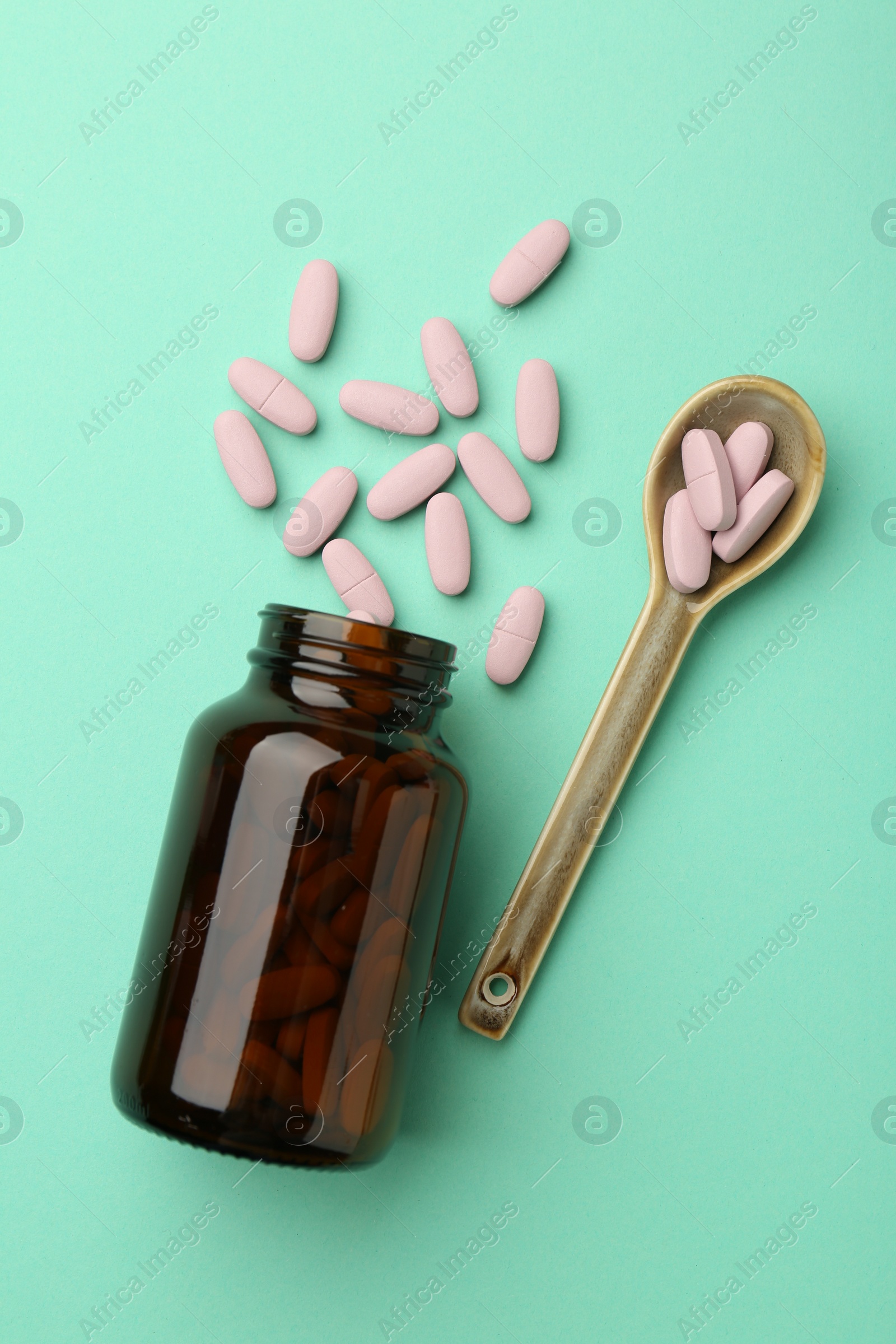 Photo of Vitamin pills, bottle and spoon on mint color background, flat lay