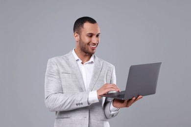 Young businessman using laptop on grey background