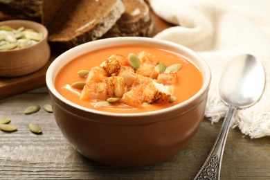 Photo of Tasty creamy pumpkin soup with croutons and seeds in bowl on wooden table