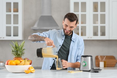 Photo of Handsome man pouring tasty smoothie into glass at white marble table in kitchen