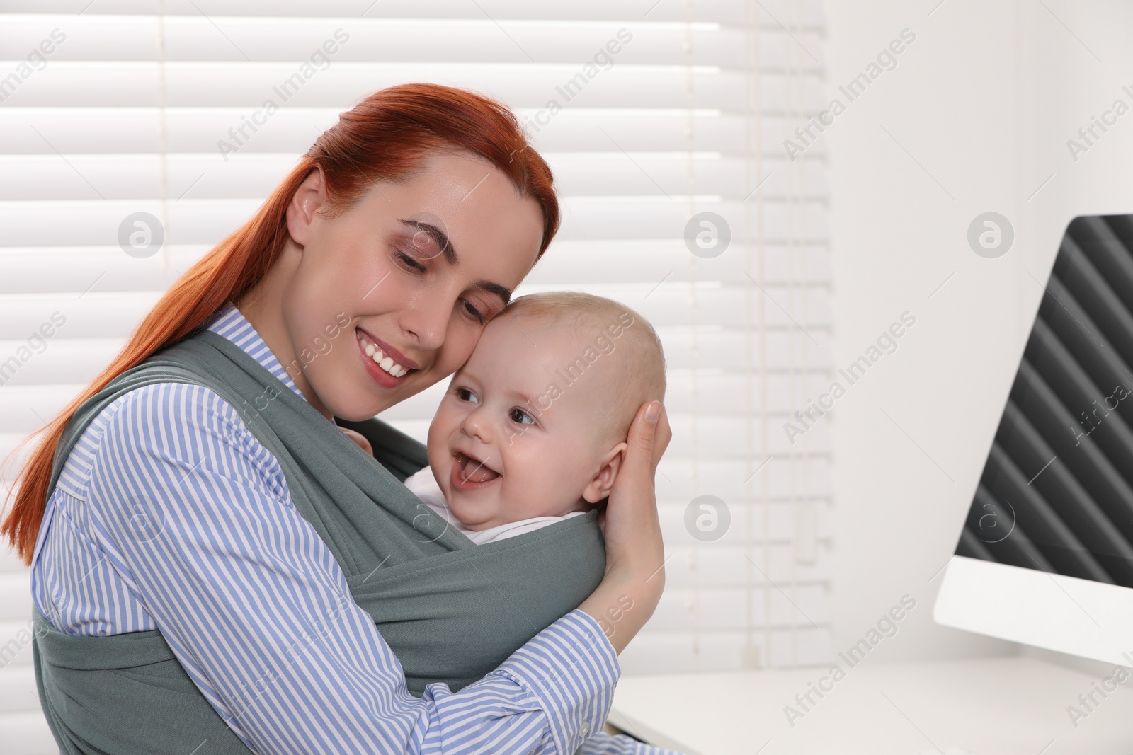 Photo of Mother holding her child in sling (baby carrier) at workplace