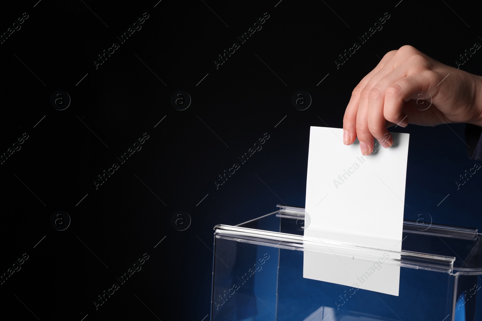 Photo of Woman putting her vote into ballot box on dark blue background, closeup. Space for text