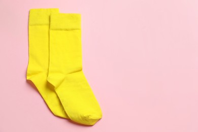 Photo of Yellow socks on light pink background, top view. Space for text