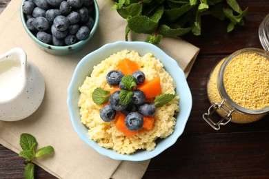 Photo of Tasty millet porridge with blueberries, pumpkin and mint in bowl on wooden table, flat lay