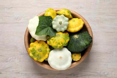 Photo of Fresh ripe pattypan squashes in bowl on light wooden table, top view