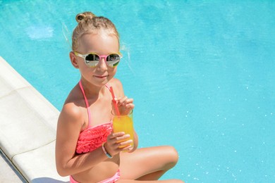 Photo of Cute little girl with glass of juice in swimming pool on sunny day. Space for text