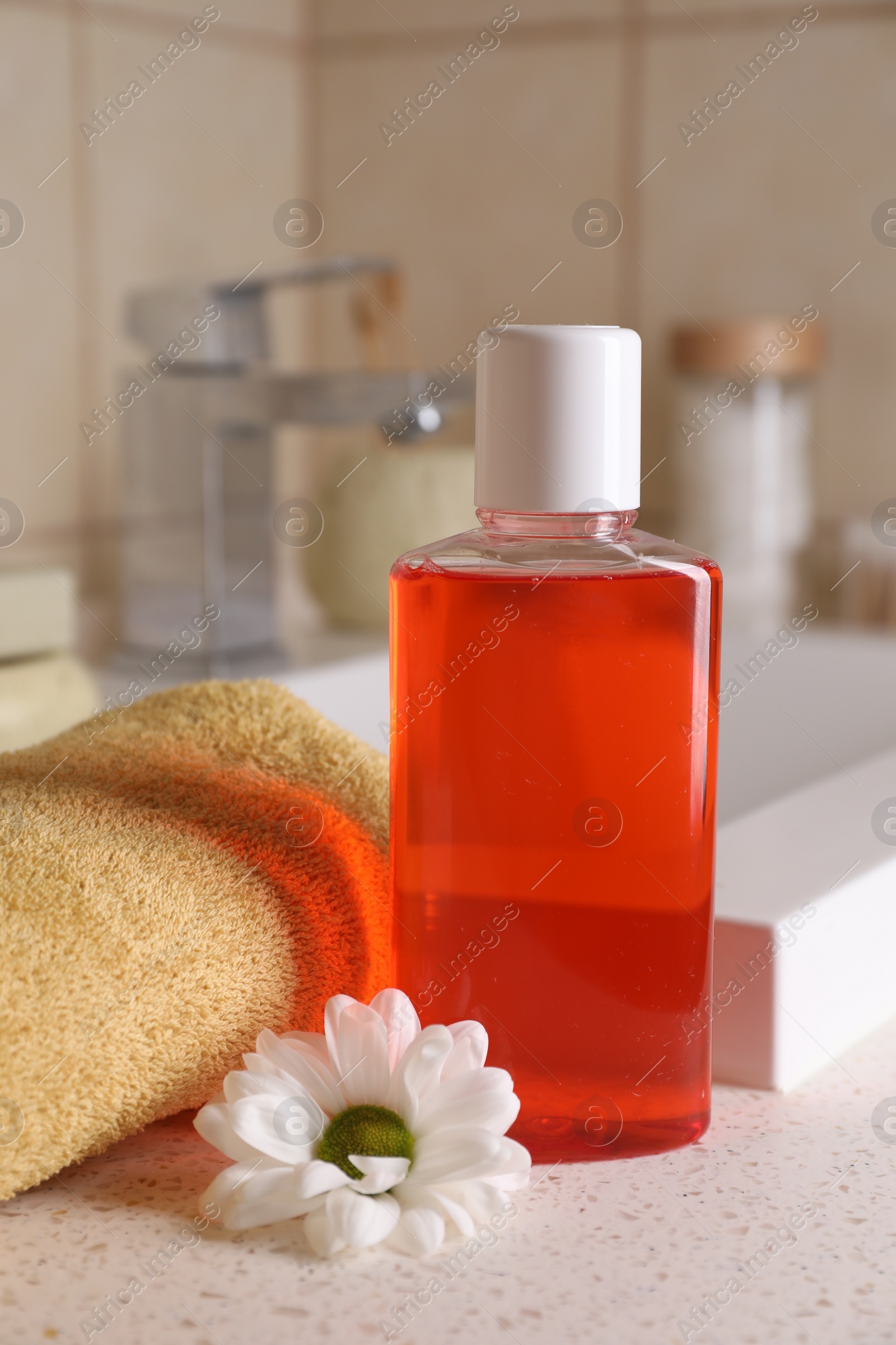 Photo of Fresh mouthwash in bottle, chamomile and towel on countertop near sink in bathroom, closeup