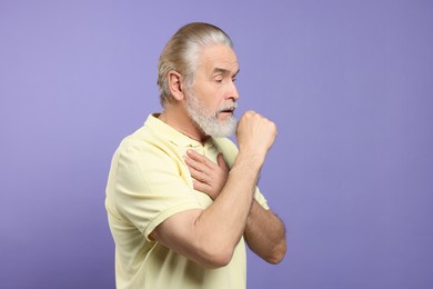 Senior man coughing on light purple background. . Sore throat