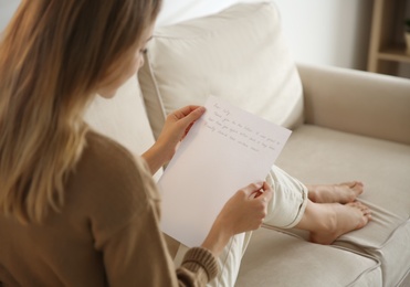 Woman reading letter on sofa at home, closeup