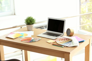 Designer's workplace with laptop and paint color palette samples on table