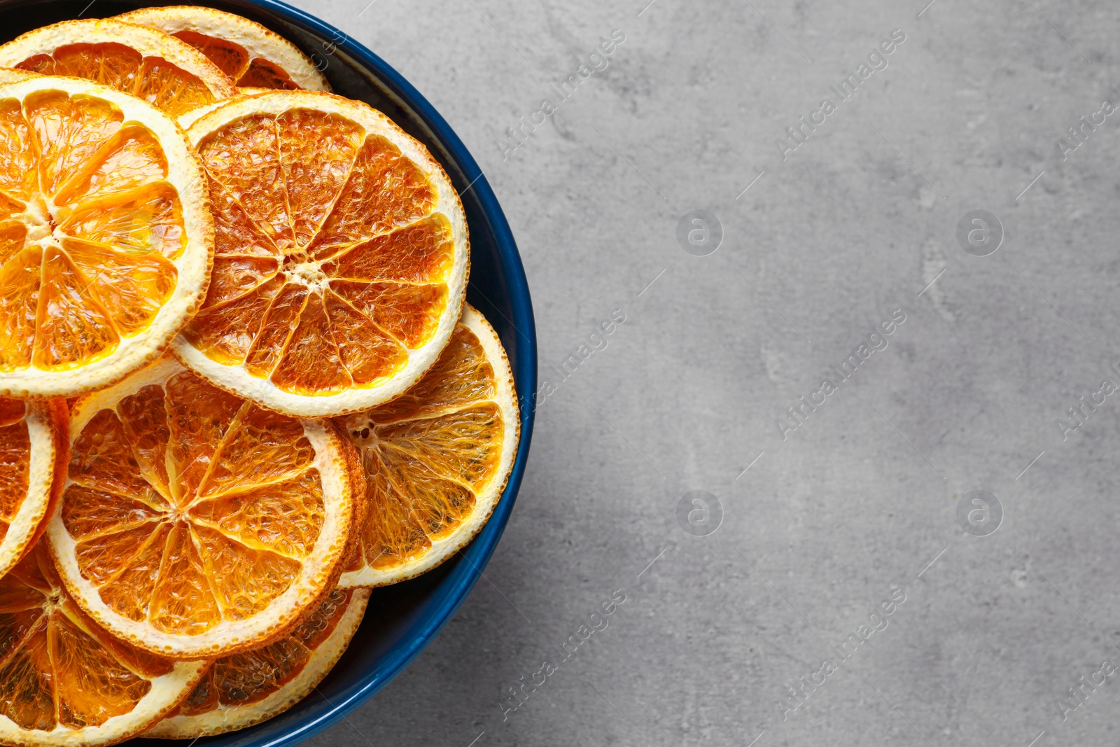 Photo of Bowl of dry orange slices on grey table, top view. Space for text