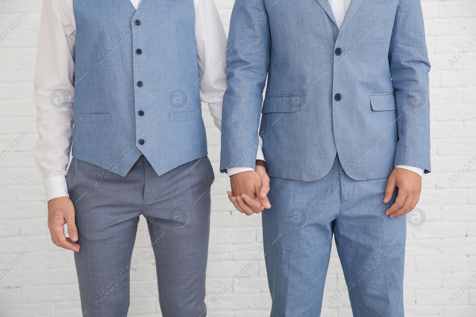 Photo of Newlywed gay couple holding hands near white wall, closeup