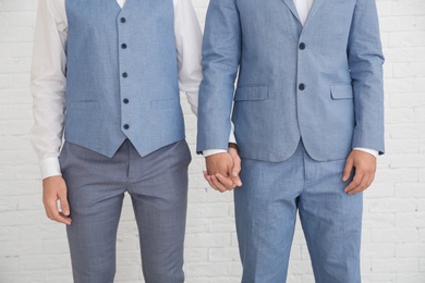 Newlywed gay couple holding hands near white wall, closeup