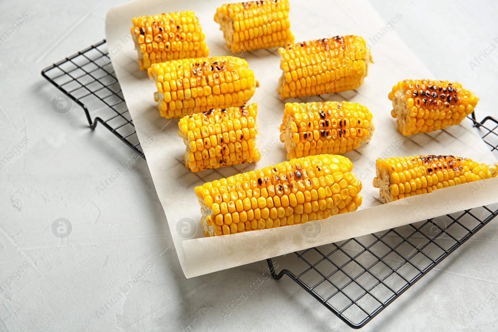 Photo of Cooling rack with grilled corn cobs on light background