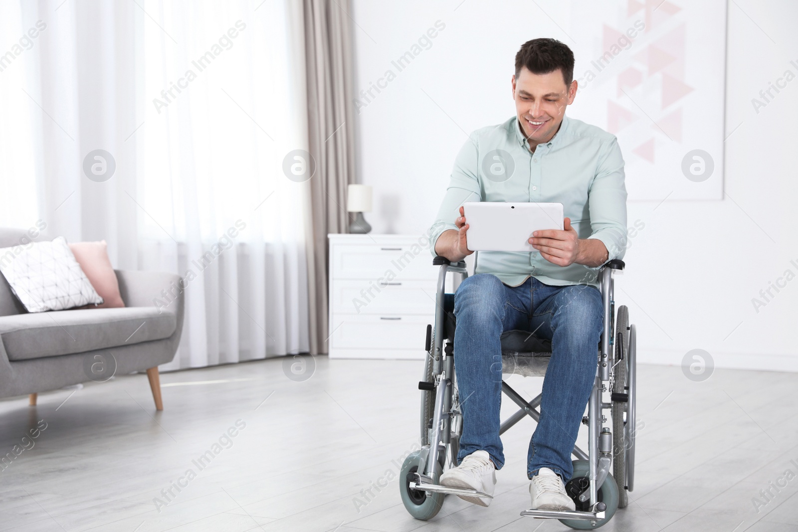 Photo of Happy man with tablet sitting in wheelchair at home