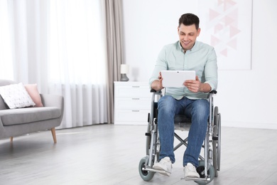 Happy man with tablet sitting in wheelchair at home