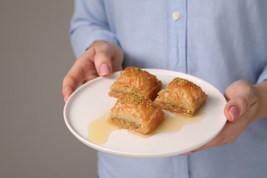 Photo of Woman with plate of delicious sweet baklava on grey background, closeup