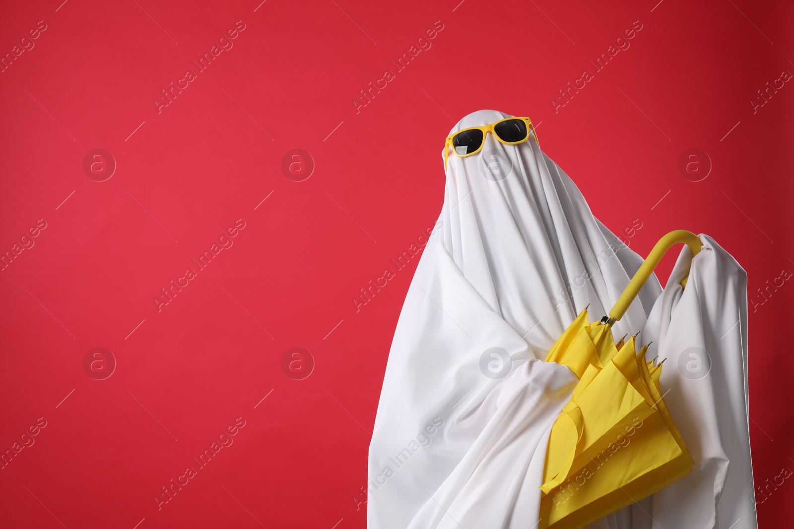 Photo of Person in ghost costume and sunglasses holding yellow umbrella on red background, space for text