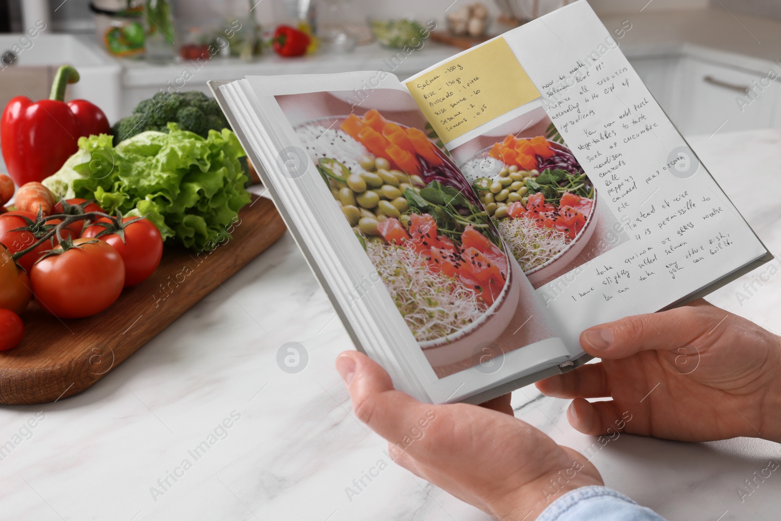 Photo of Man with recipe book at white marble table in kitchen, closeup