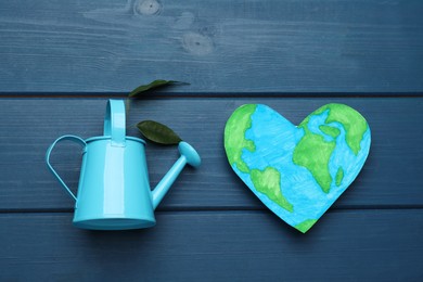 Photo of Happy Earth Day. Heart shaped plasticine planet and watering can with plant on blue wooden table, flat lay