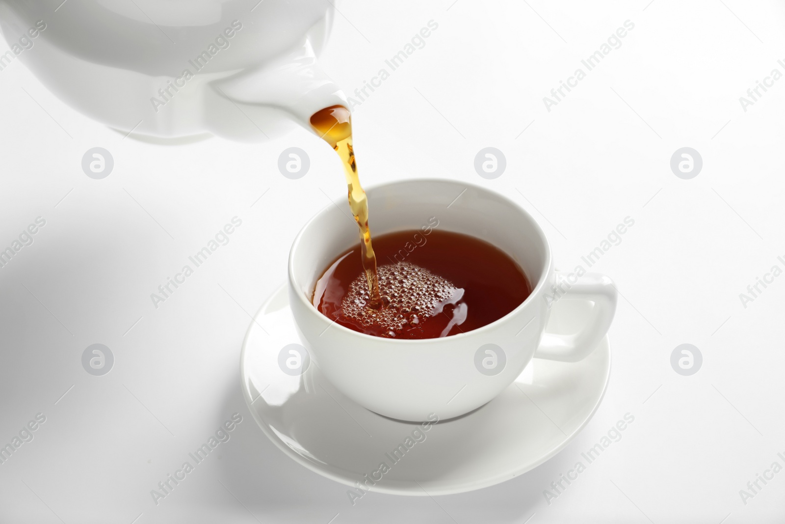 Photo of Pouring hot tea into porcelain cup on white background