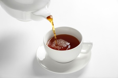 Pouring hot tea into porcelain cup on white background