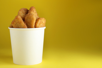 Bucket with tasty chicken nuggets on yellow background. Space for text