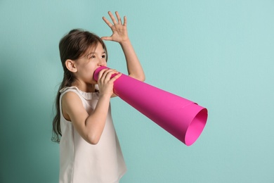 Adorable little girl with paper megaphone on color background