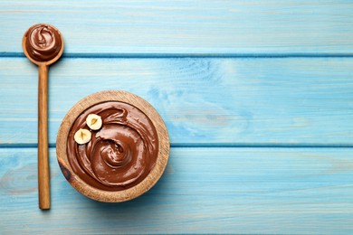 Spoon and bowl of tasty chocolate hazelnut spread on light blue wooden table, flat lay. Space for text