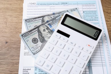 Photo of Tax accounting. Calculator, document and dollar banknotes on wooden table, closeup