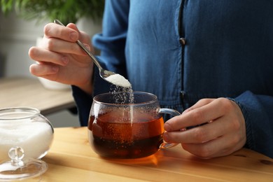 Woman adding sugar into aromatic tea at wooden table indoors, closeup