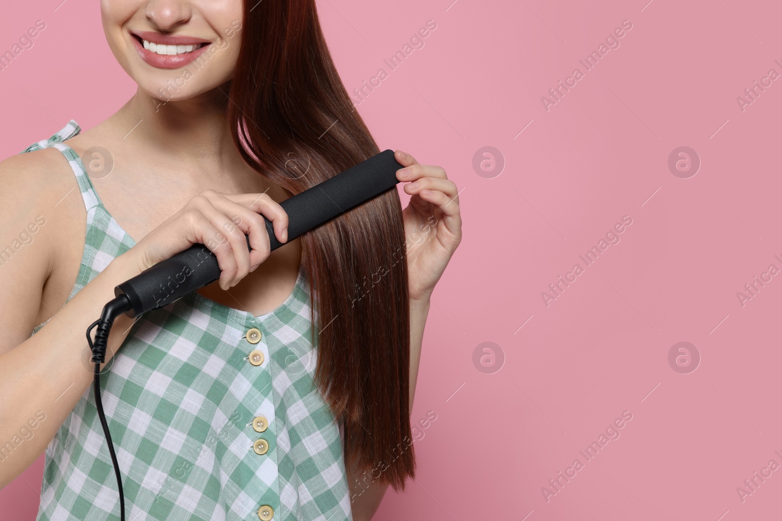 Photo of Woman with hair iron on pink background, closeup. Space for text