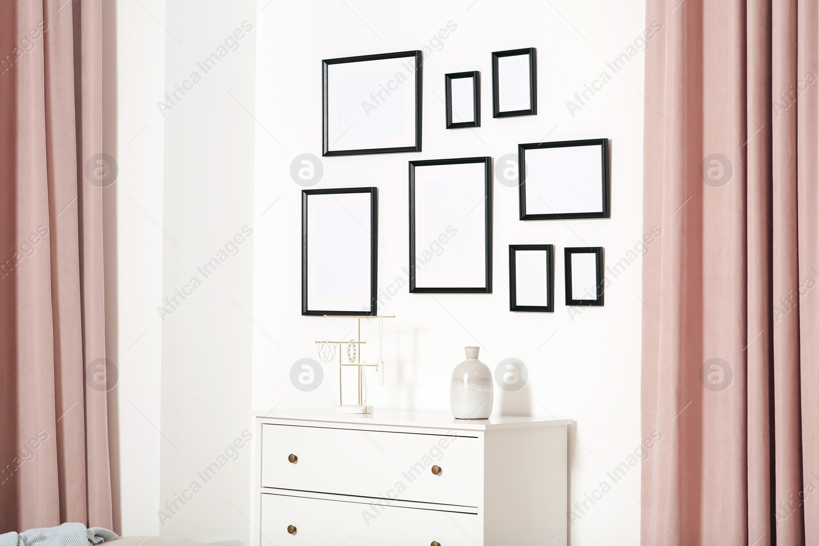 Photo of Empty frames hanging on white wall and chest of drawers indoors