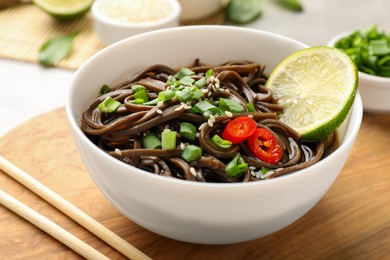 Photo of Tasty buckwheat noodles (soba) with sauce, onion in bowl and chopsticks on table, closeup