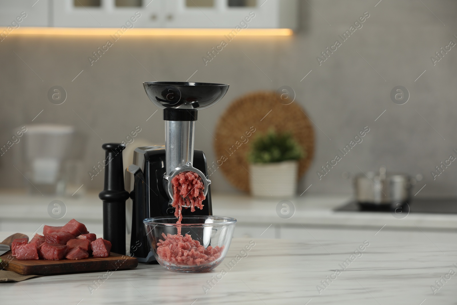 Photo of Electric meat grinder with beef mince on white table in kitchen, space for text