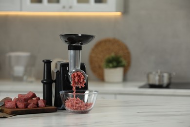 Electric meat grinder with beef mince on white table in kitchen, space for text