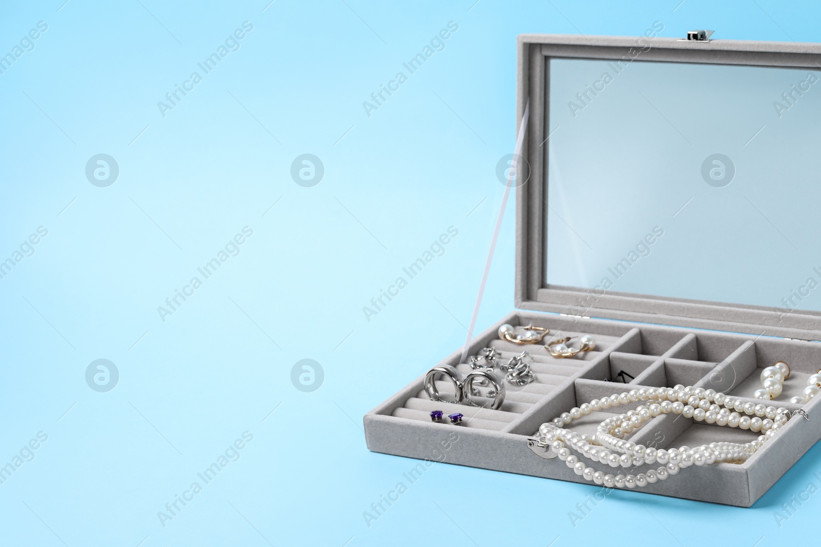Photo of Jewelry box with many different accessories on light blue background, space for text