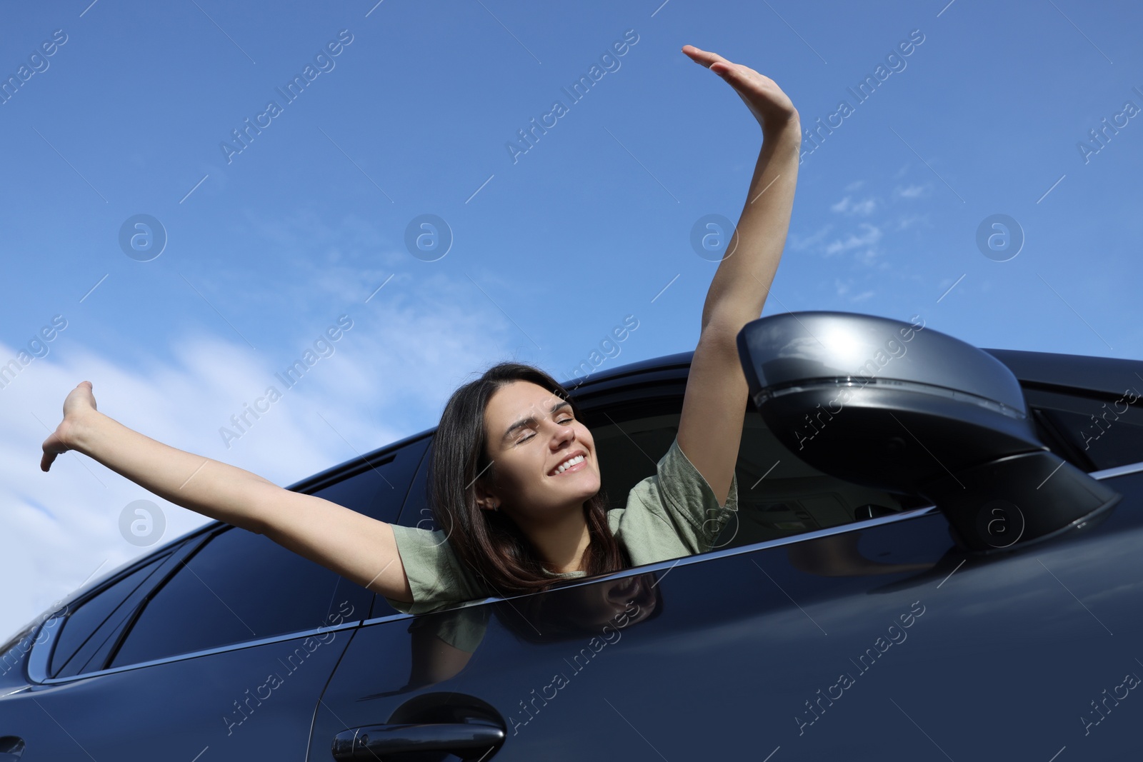 Photo of Beautiful young woman raising arms from car window