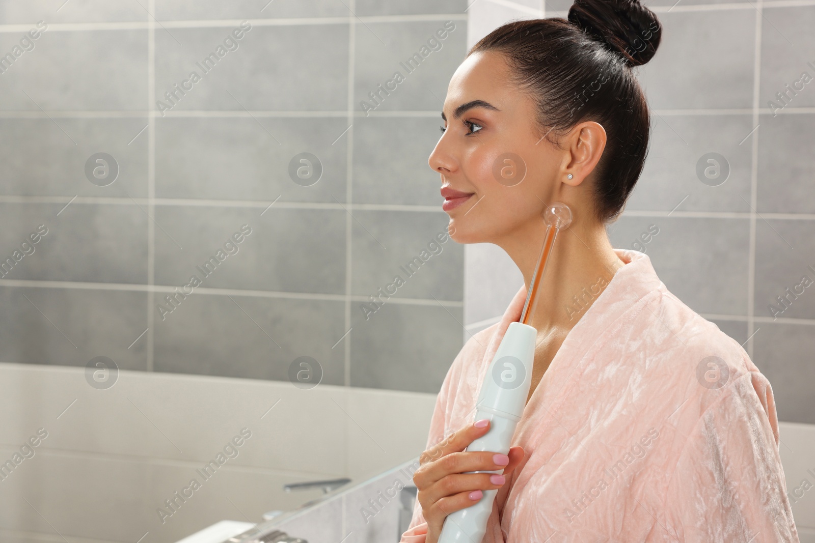 Photo of Woman using high frequency darsonval device in bathroom, space for text