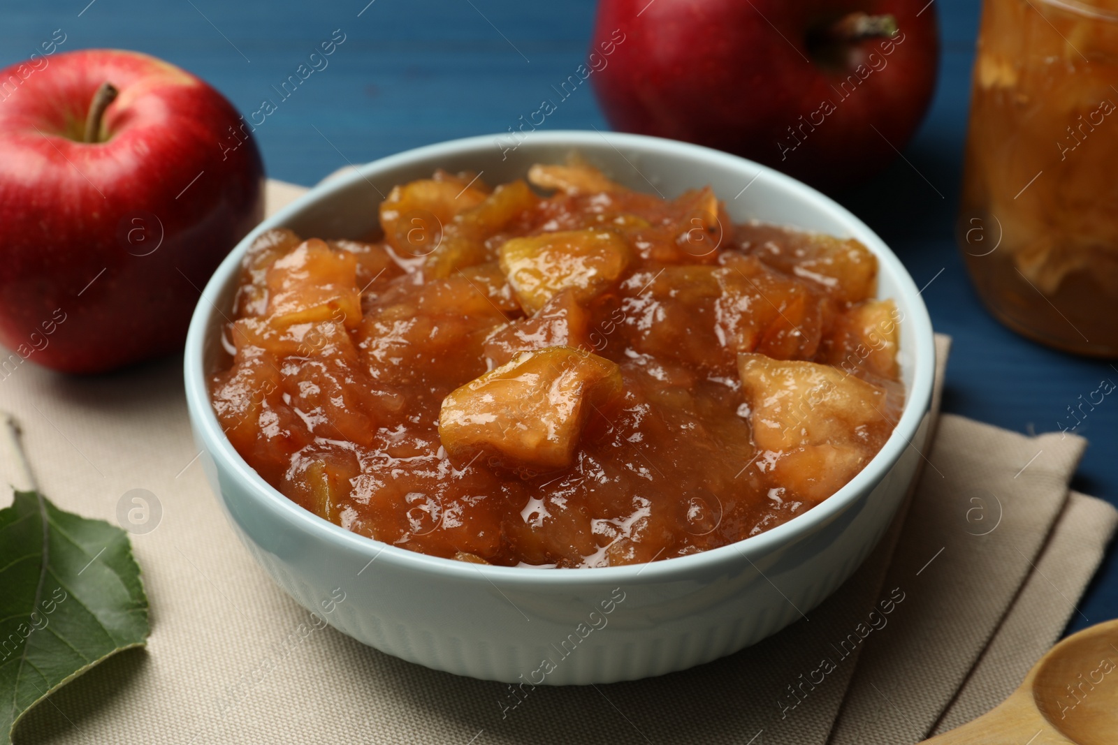 Photo of Tasty apple jam in bowl and fresh fruit on blue table, closeup