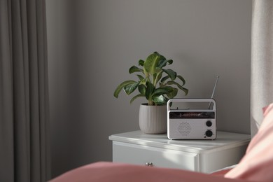 Photo of Stylish radio receiver and plant on nightstand in bedroom