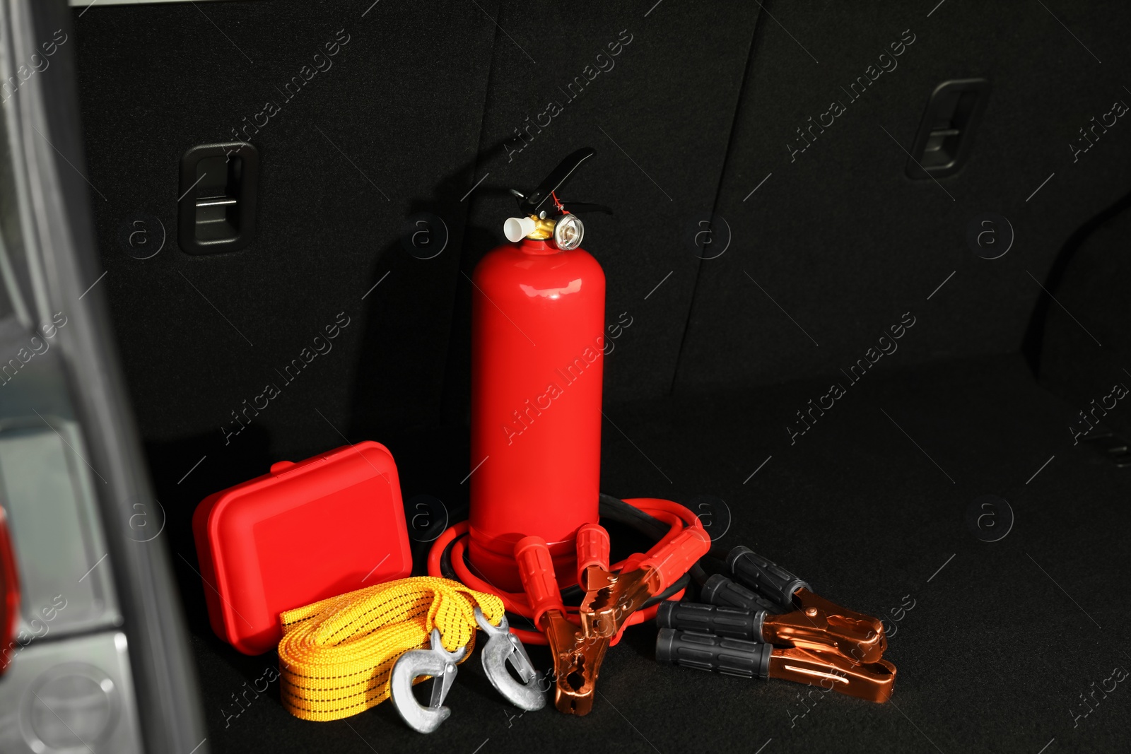 Photo of Red fire extinguisher, battery jumper cables, towing strap and first aid kit in trunk, space for text. Car safety