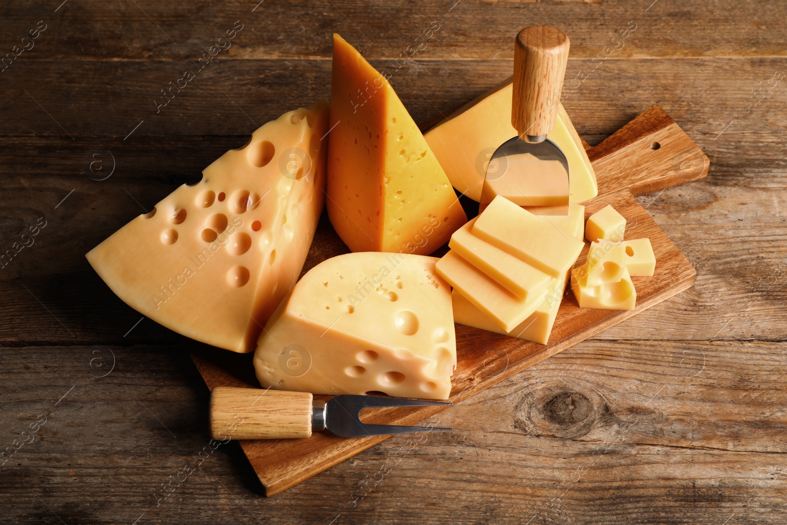 Photo of Different sorts of cheese, fork and knife on wooden table