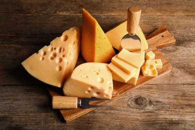 Different sorts of cheese, fork and knife on wooden table