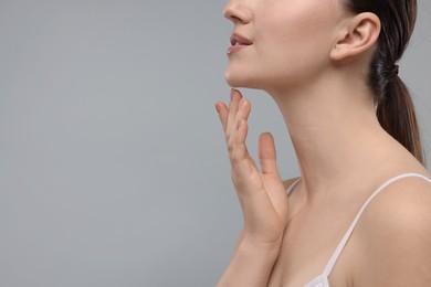 Woman touching her chin on grey background, closeup. Space for text