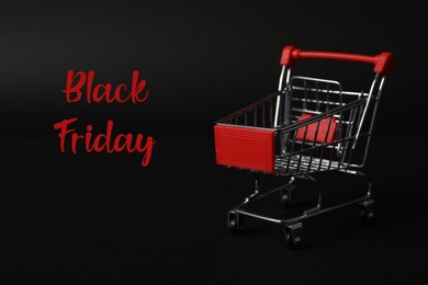Photo of Phrase Black Friday and toy shopping cart on dark background
