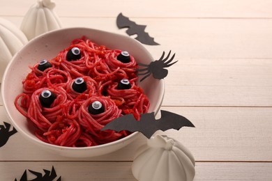 Red pasta with decorative eyes in bowl and Halloween decorations on white wooden table, closeup. Space for text