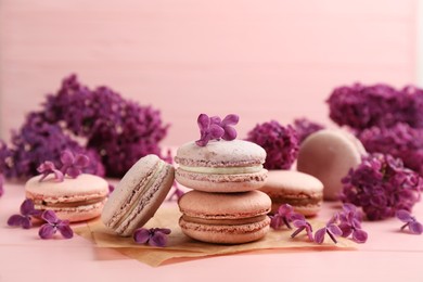 Photo of Delicious macarons and flowers on pink wooden table
